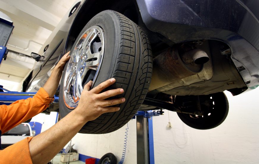 Meccanico al lavoro su una ruota sollevata sul ponte in officina a Cremona